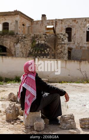 Hama, Syrien 04-02-2010: Ein junger arabischer Mann mit Keffiyeh und schwarzem jubba-Kleid sitzt auf einem Felsen in der Altstadt von Hama und Stockfoto