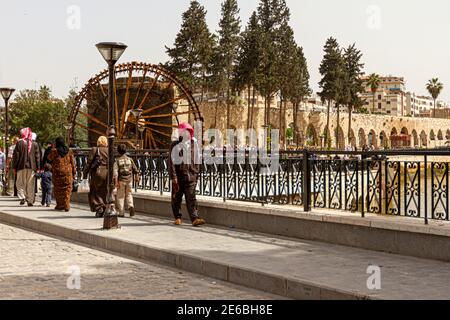 Hama, Syrien 04-02-2010: Stadtbild der historischen Stadt Hama mit einer Brücke über den Fluss Orontes, wo Menschen in ethnischer Kleidung spazieren gehen. In Th Stockfoto