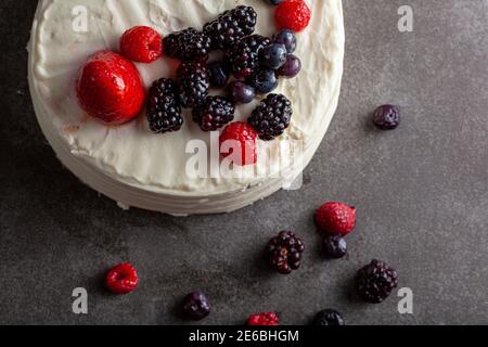 Nahaufnahme flach Lay Low-Light-Bild eines runden Kuchen mit cremig weißen Glasur und Auswahl an Beeren als dekorative Beläge verwendet. Serviert auf dunkelgrau b Stockfoto