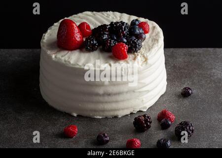 Nahaufnahme abgewinkelte Ansicht Bild von einem runden Kuchen mit cremig-weißen Glasur und Auswahl von Beeren als dekorative Beläge verwendet. Serviert auf dunkelgrauer schwarzer Ba Stockfoto