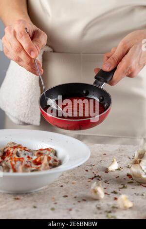 Eine Küchenchefin trägt Schürze fügt frische Tomatensauce zu hausgemachten türkischen Knödel in Joghurt. Dieses traditionelle Gericht ist als Manti bekannt und wird serviert Stockfoto