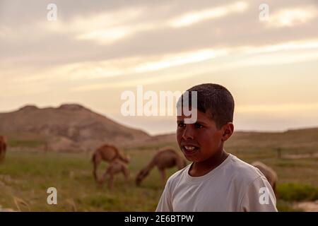 Wadi Musa, Jordanien 04.01.2010: Porträt eines jungen gebräunten lokalen Beduin Kamelhirten Jungen, der von seinen Kamelen auf trockenen jordanischen Hügeln wartet. Im Blurr Stockfoto