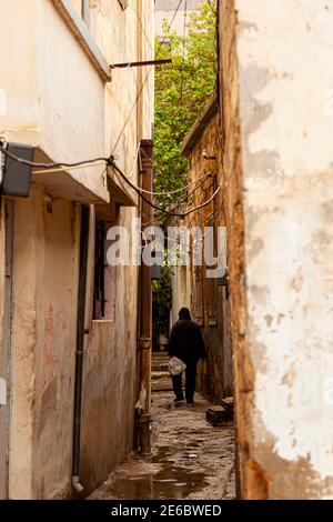 Eine schmale Gasse in einem einkommensschwachen alten Stadtviertel in Damaskus, Syrien. Die Häuser sind heruntergekommen und die Kabel hängen zwischen den Gebäuden. Regen p Stockfoto