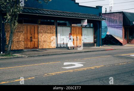 Junge Frau geht an einem vernagelten Gebäude in Tacoma vorbei Frühjahr 2020 während der ersten Phase der Geschäftsschließungen fällig Zur Pandemie Covid-19 Stockfoto