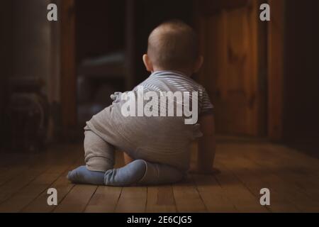 Kleiner lustiger kleiner Junge, der lernt, auf Holzboden zu kriechen. Selektiver Fokus. Rückansicht. Familienleben. Stockfoto
