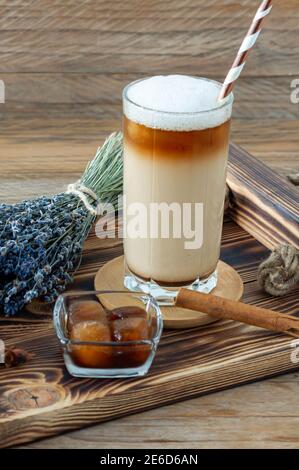 Latte oder Cappuccino mit Milchschaum und Lavendel in einem hohen Glas auf Holztablett Stockfoto