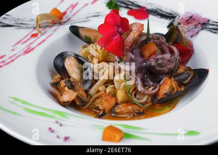 Pasta mit Garnelen, Muscheln und Tintenfisch in Sauce, auf einem weißen Teller Stockfoto