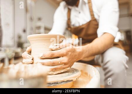 Ein junger männlicher Töpfer arbeitet in seiner Werkstatt an einem Töpferrad und stellt Tonprodukte her. Nahaufnahme der Hände Stockfoto
