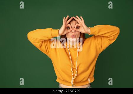 Superhelden. Kaukasische Frau Porträt isoliert auf grünem Studio-Hintergrund mit Copyspace. Schönes weibliches Modell in gelbem Sweatshirt. Konzept der menschlichen Emotionen, Gesichtsausdruck, Verkauf, Werbung, Mode. Stockfoto