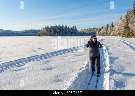 Frauen im Ruhestand Skifahren auf einer Schneemobilstrecke auf einem gefrorenen See mit verschneiten Wald und einem blauen Himmel im Hintergrund, Bild von Vasternorrland Schweden. Stockfoto