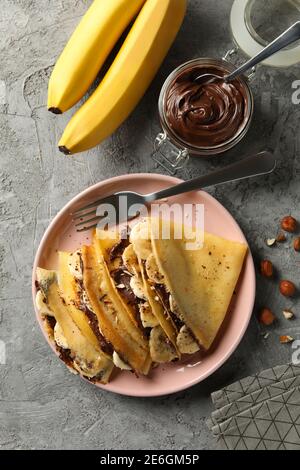 Konzept des leckeren Frühstücks mit Crepes mit Schokoladenpaste, Banane und Nüsse auf grauem Hintergrund Stockfoto