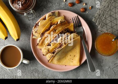 Konzept des leckeren Frühstücks mit Crepes mit Schokoladenpaste, Banane und Nüsse auf grauem Hintergrund Stockfoto