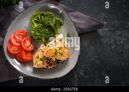 Gebratener Thunfisch mit Brokkoli und Tomaten auf einem grauen Teller und einem dunklen rustikalen Schieferhintergrund, gesunde Mahlzeit zum Abnehmen mit ketogener oder Low Carb Diät, c Stockfoto