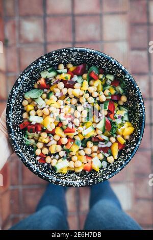 Person trägt Jeans mit einer Schüssel Kichererbsen-Salat über einem Vintage-Fliesenboden. Stockfoto