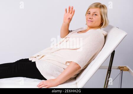 Ältere Frau, die auf einem Stuhl sitzt, taucht ihre Hand, während sie auf die Kamera schaut, während sie auf den Zahnarzt wartet. Gesundes Zahnkonzept. Stockfoto