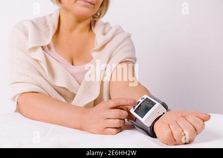 Eine ältere Frau überprüft ihren Blutdruck mit einem elektronischen Blutdruckmessgerät zu Hause. Weißer Hintergrund. Stockfoto
