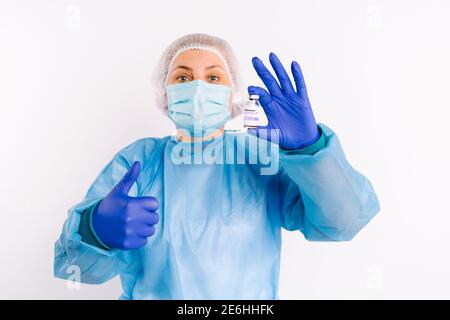 Ein Sanitäter in einer Schutzwache schaut auf die Kamera, die die Klasse zeigt und hält einen Impfstoff aus Covid 19 in den Händen. Weißer Hintergrund. Daumen hoch. Stockfoto