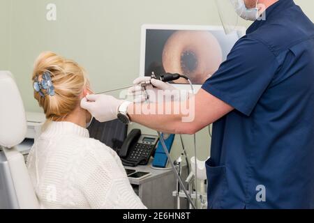 Otolaryngologe tut Otitus Untersuchung, Video-Otoskopie Verfahren. Hörklinik. HNO-Arzt mit Werkzeugen, die Maske und Handschuhe tragen, untersucht den Patienten Stockfoto