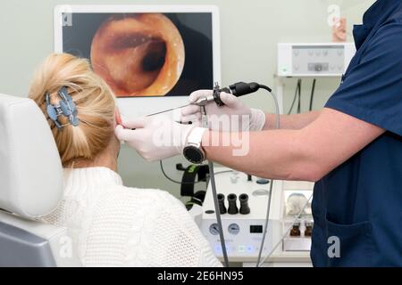 Otolaryngologe tut Otitus Untersuchung, Video-Otoskopie Verfahren. Hörklinik. HNO-Arzt mit Werkzeugen, die Maske und Handschuhe tragen, untersucht den Patienten Stockfoto