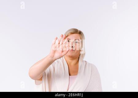 Die blonde Frau zeigt ihre leere Handfläche der Kamera. Stoppen oder Ablehnen eines Fotos vor einem weißen Hintergrund mit seitlichem Leerzeichen. Stockfoto