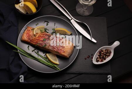 Gegrillter oder gebratener Lachs mit Kräutern, Knoblauch, Gewürzen und Zitrone auf dunklem Hintergrund. Gesunde Ernährung. Draufsicht. Stockfoto