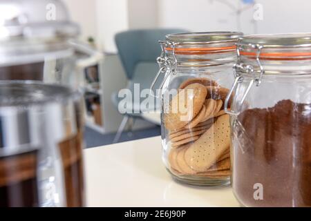 Eine moderne Büroküche mit Keksen in einem Kilner-Glas auf einer weißen Arbeitsplatte mit modernen Möbeln im Hintergrund. Stockfoto