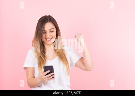 Eine junge blonde Frau, die ihr Handy anschaut, macht Eine Geste des Sieges Stockfoto