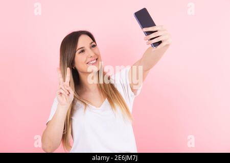 Eine junge blonde Frau macht ein Selfie mit ihrem Handy Telefon macht eine Siegesgeste Stockfoto
