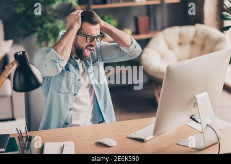 Foto Porträt von unglücklichen Mann schreien auf Desktop-Bildschirm halten Kopf mit zwei Händen am Tisch im modernen Industriebüro In Innenräumen Stockfoto