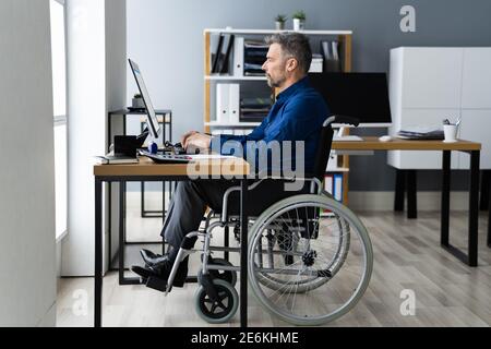 Behinderter Behinderter Mann Im Rollstuhl, Der Mit Computertechnologie Arbeitet Stockfoto