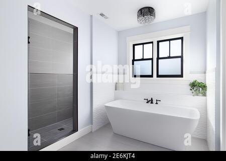 Ein wunderschönes, luxuriöses Badezimmer mit einem Licht, das über einer weißen Fleurco-Badewanne hängt und einem schwarzen Wasserhahn, der von Fliesen und einer Marmordusche umgeben ist. Stockfoto