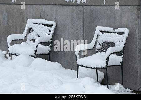 Zwei Rattanstühle links neben dem Gebäude unter Schneefall Stockfoto