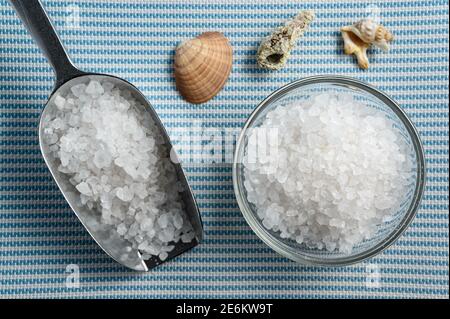 Metallic Schaufel und Glasschale voller Meersalz auf Weiße und blaue Matten mit Muscheln Stockfoto