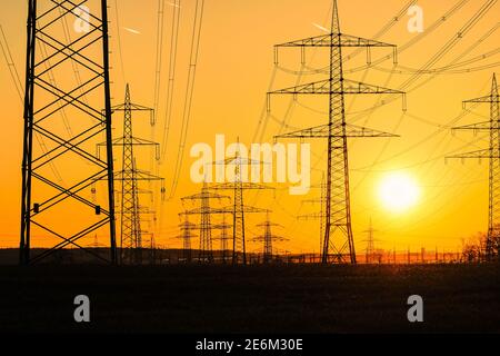 Strommasten und Stromübertragungsleitungen gegen den vibrierenden orangefarbenen Himmel bei Sonnenuntergang an einem heißen Tag mit flackernder Luft. Hochspannungstürme pro Stockfoto