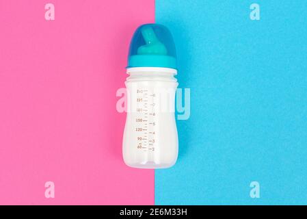 Babyflasche mit weißer Milch auf rosa blauem Tischhintergrund. Babyfütterung Konzept. Nahaufnahme. Draufsicht Stockfoto