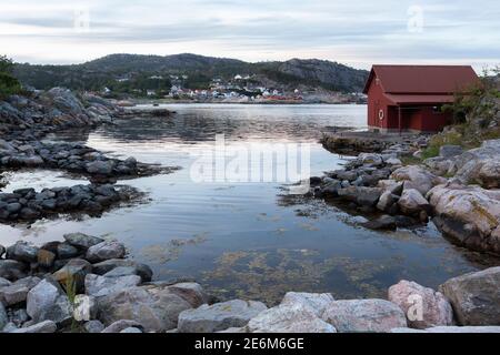 Rotes Bootshaus auf einer kleinen Halbinsel bei Sonnenuntergang an der Küste von Lindesnes, Norwegen Stockfoto