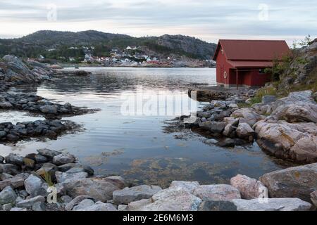 Rotes Bootshaus auf einer kleinen Halbinsel bei Sonnenuntergang an der Küste von Lindesnes, Norwegen Stockfoto