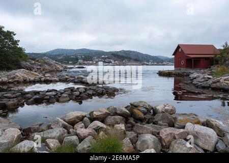 Rotes Bootshaus auf einer kleinen Halbinsel bei Sonnenuntergang an der Küste von Lindesnes, Norwegen Stockfoto