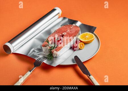 Frischer Lachs mit Zitrone in Folienpapier, fertig zum Kochen im Ofen auf orangefarbenem Hintergrund. Stockfoto