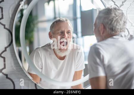 Mann macht lustige Gesichter in der Nähe des Spiegels Stockfoto