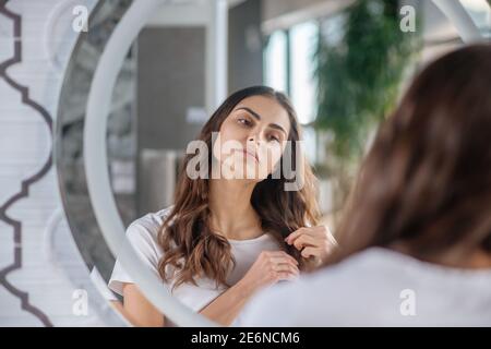 Frau überprüft ihre Haarspitzen in der Nähe des Spiegels Stockfoto