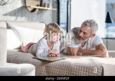 Grauhaariger Mann beim Lesen von Kinderbuch und Kind Stockfoto