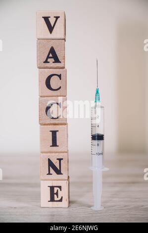 Word Text IMPFSTOFF aus Holzwürfeln und Spritze isoliert auf einem Holztisch Hintergrund mit Kopierraum. Medizinisches Konzept. Stockfoto