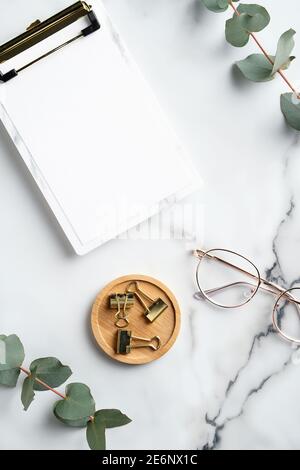 Eleganter femininer Arbeitsplatz mit Klemmbrett, Bürobedarf, Brille auf Marmorhintergrund. Home Office Schreibtisch, Tischansicht von oben. Stockfoto