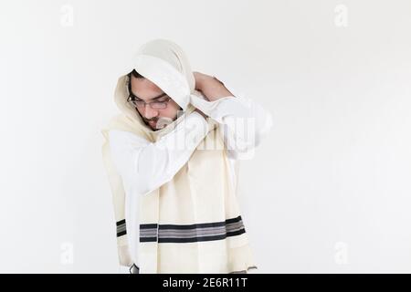 Junger orthodoxer Kaukasusmann, der seinen Schal gegen Weiß aufsetzt Wand Stockfoto