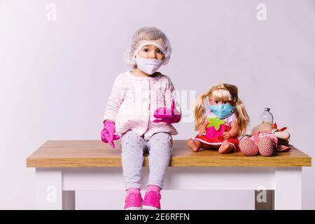 Kleines Mädchen in einer medizinischen Maske und rosa Latexhandschuhe mit Spielzeug auf weißem Hintergrund. Kinderklinik und Ansatz für junge Patienten. Stockfoto