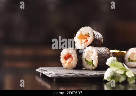 Detail von verschiedenen Sushi Maki auf Schieferteller und Essstäbchen auf schwarzem Holztisch. Vorderansicht. Horizontale Zusammensetzung. Stockfoto