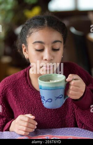 Nahaufnahme des elfjährigen Biracial Mädchens, das auf heißen Kakao bläst Stockfoto