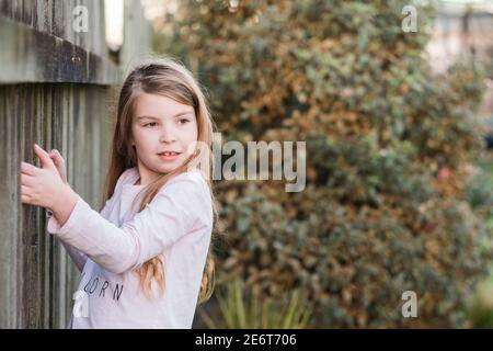 Junges Mädchen steht und hält auf Holzzaun Stockfoto