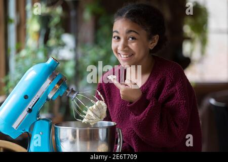 Ein elfjähriges Biracial Mädchen schleicht sich einen Geschmack von Schlagsahne Creme Stockfoto